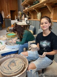Girl on pottery wheel with pottery teacher